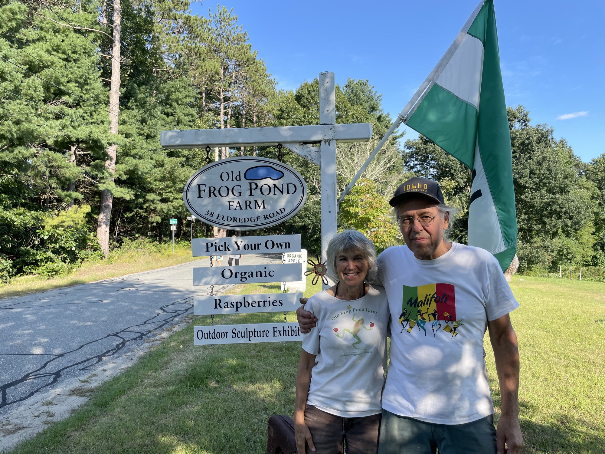 Owners of Old Frog Pond Farm stand in front of their sign.